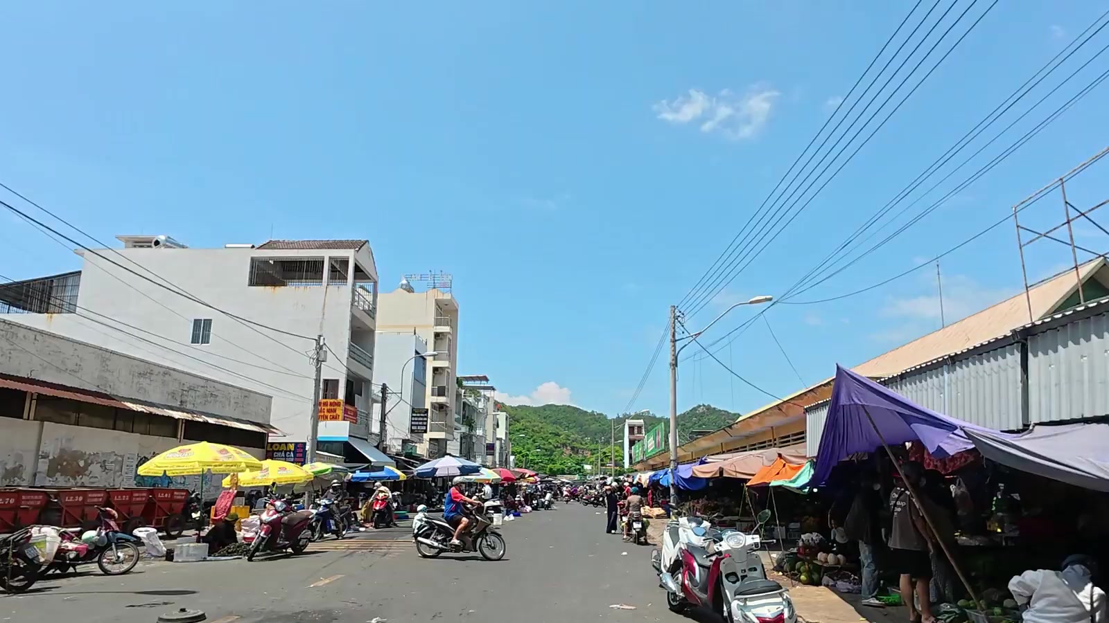 Chợ Vĩnh Hải Nha Trang nhìn từ đường Củ Chi, sạp hàng che dù họp hai bên đường, cách lô đất vài chục mét
