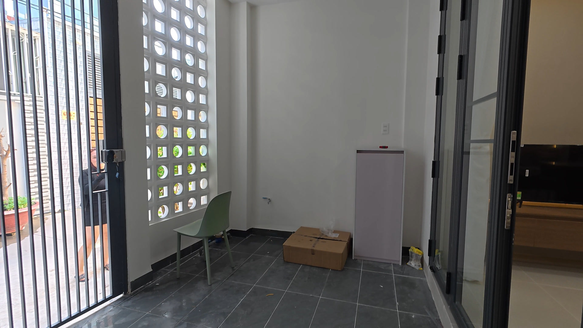 Chỗ để xe trong nhà của căn hộ tầng 1 nhà Ngô Đến, sàn lát gạch, cổng sắt ra hẻm và mảng gạch bông gió lấy sáng