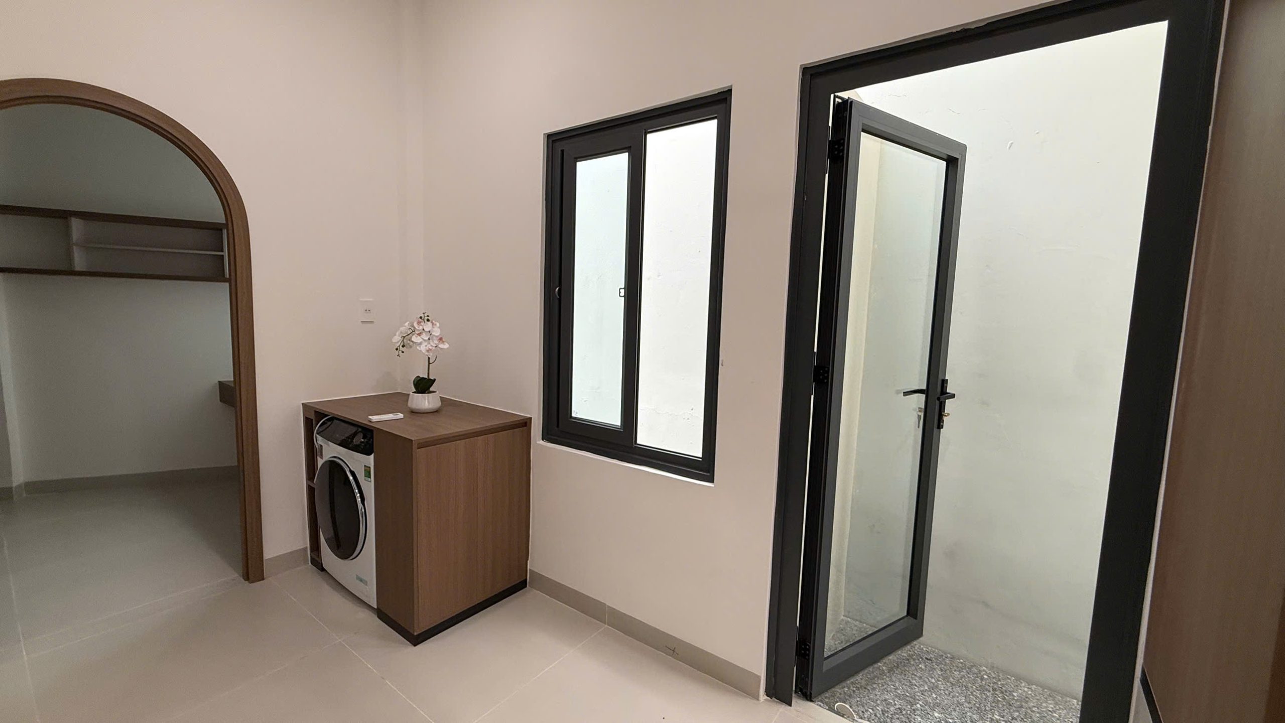 Khu giặt nhà Ngô Đến với máy giặt đặt dưới mặt bàn gỗ, cửa kính mở ra giếng trời lấy sáng phía sau