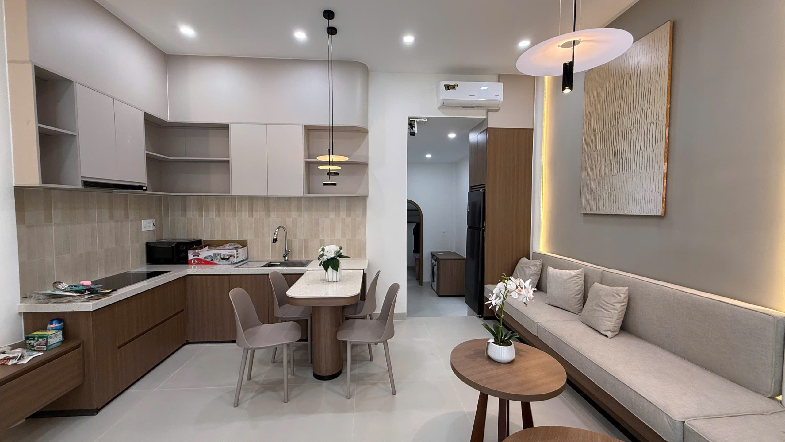 Phòng khách liền bếp căn hộ tầng 2 nhà Ngô Đến, bếp chữ L mặt đá, bàn ăn và sofa dài