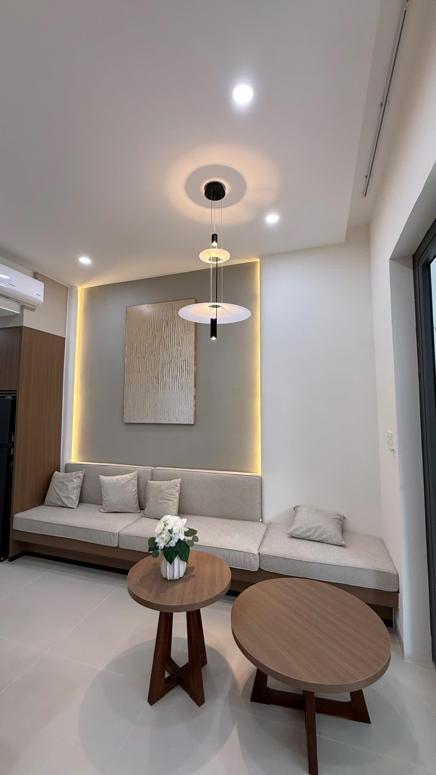 Phòng khách căn hộ tầng 2 với sofa dài đóng liền tường, tranh và đèn thả, hắt sáng quanh mảng tường