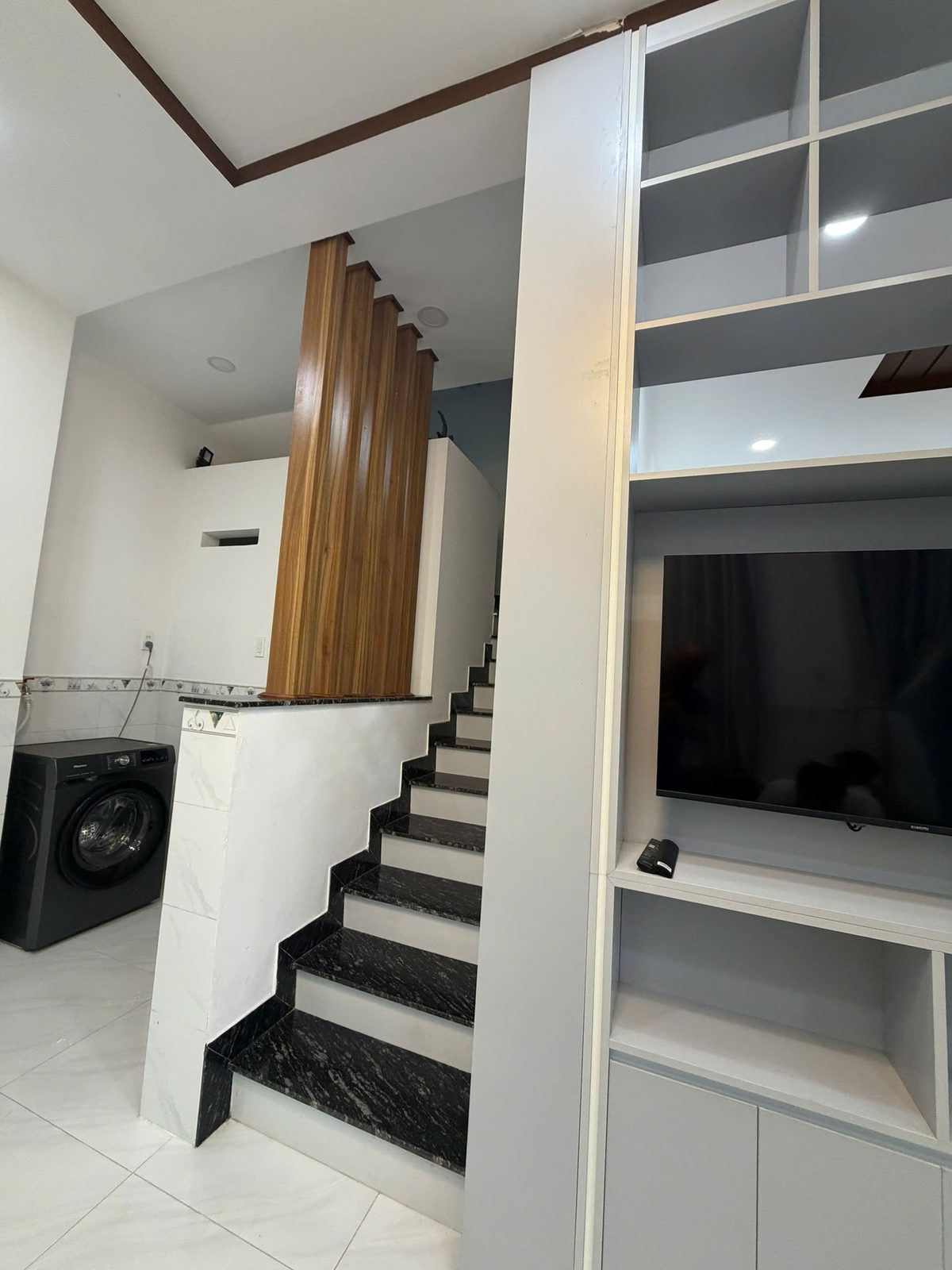 Cầu thang lát đá đen dẫn lên tầng trên của nhà Vĩnh Điềm, bên phải là kệ tivi âm tường, phía sau là khu giặt có máy giặt